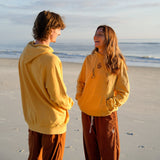 Two people in yellow hoodies standing on a beach with ocean and sky in the background