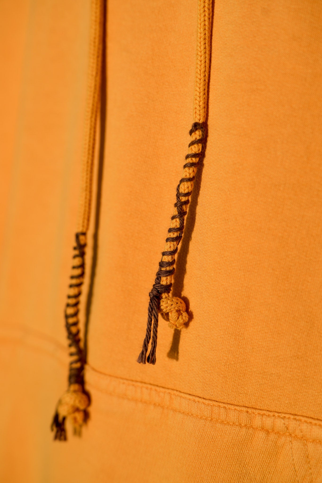 Close-up of orange fabric with braided drawstrings on a matching background