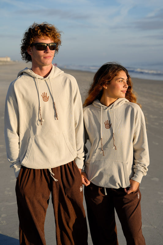 Two people wearing matching light gray hoodies with a hand design on a beach.