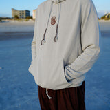 Person wearing a light gray hoodie with a logo on a beach