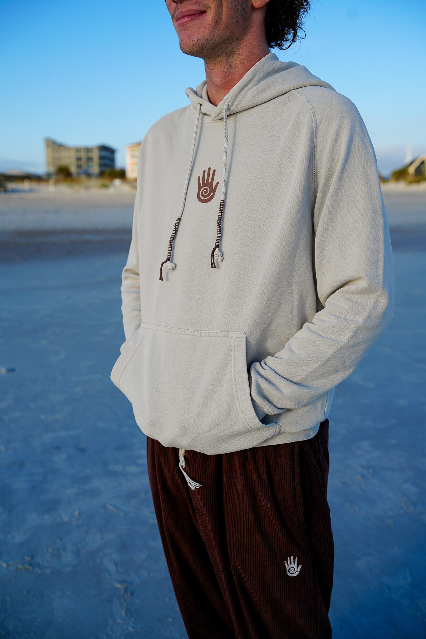 Person wearing a light gray hoodie with a logo on a beach
