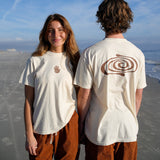 Two people standing on a beach wearing white t-shirts with hand and spiral designs.