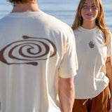 Two people wearing white t-shirts with unique designs, standing by a body of water.