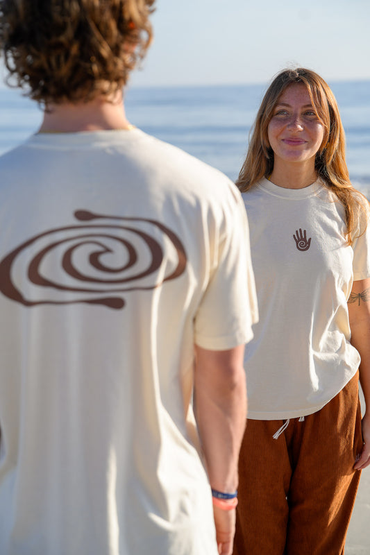 Two people wearing white t-shirts with unique designs, standing by a body of water.