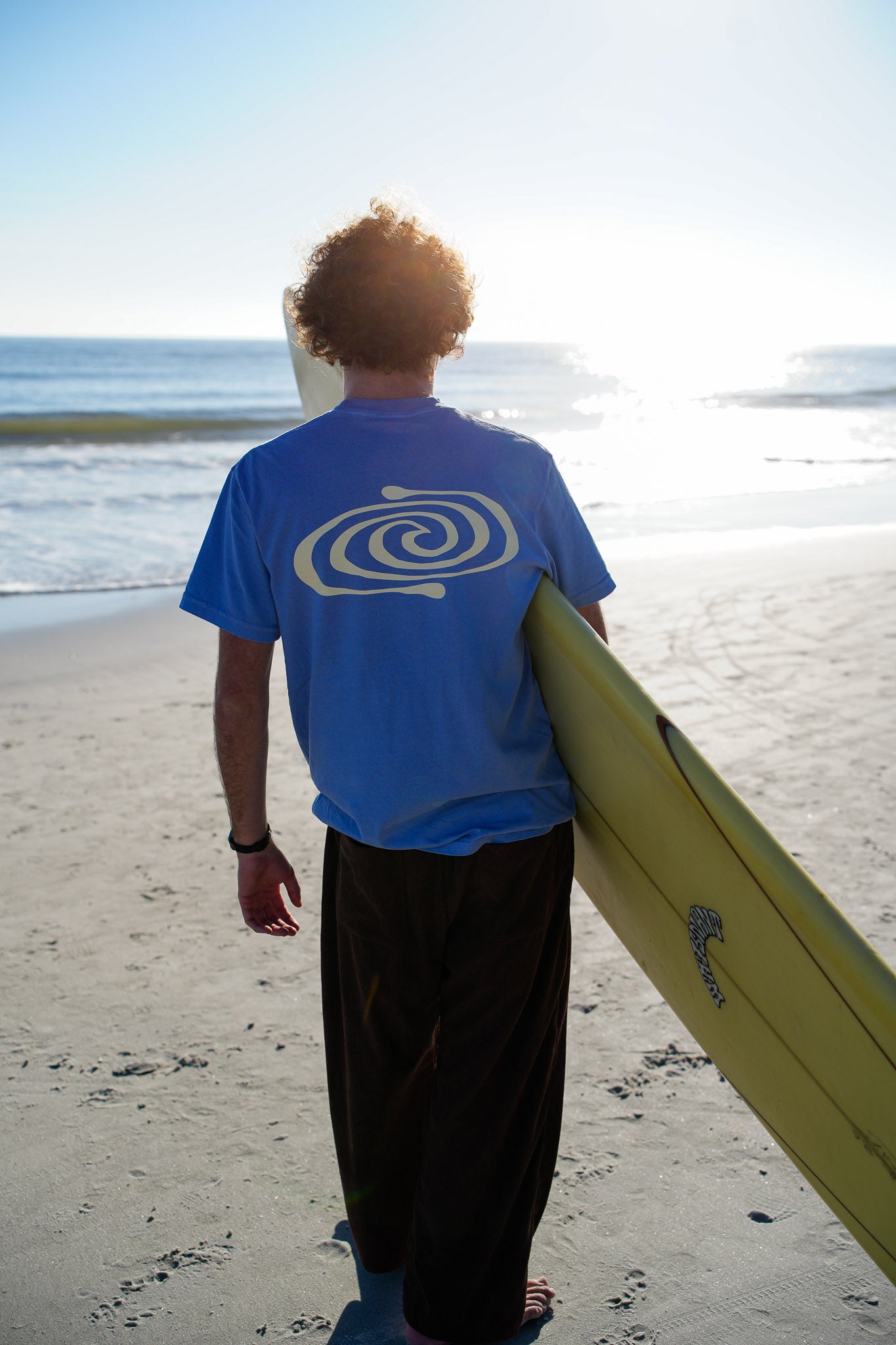 Person holding a surfboard on a beach with a blue sky and ocean in the background