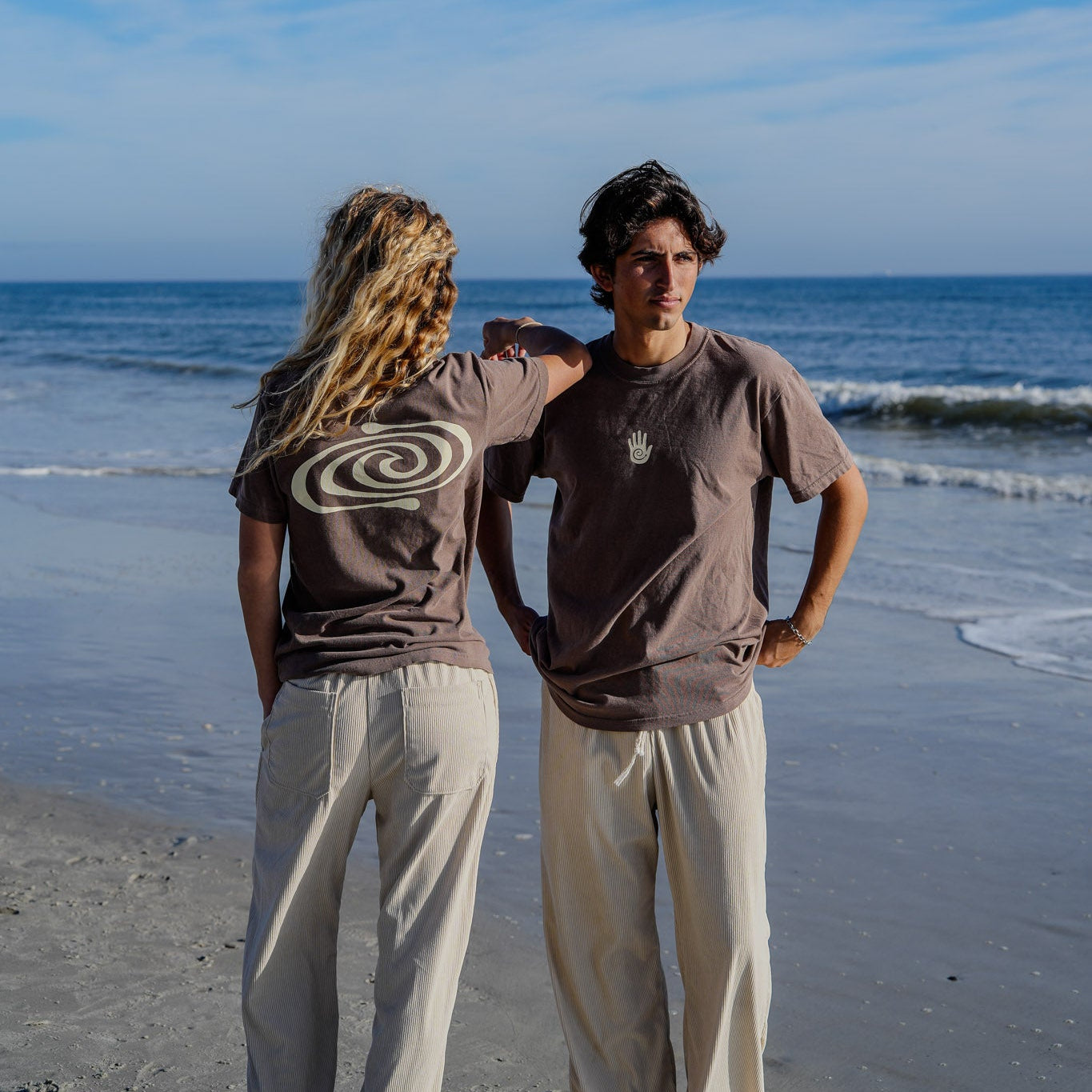 Two people standing on a beach with ocean waves in the background