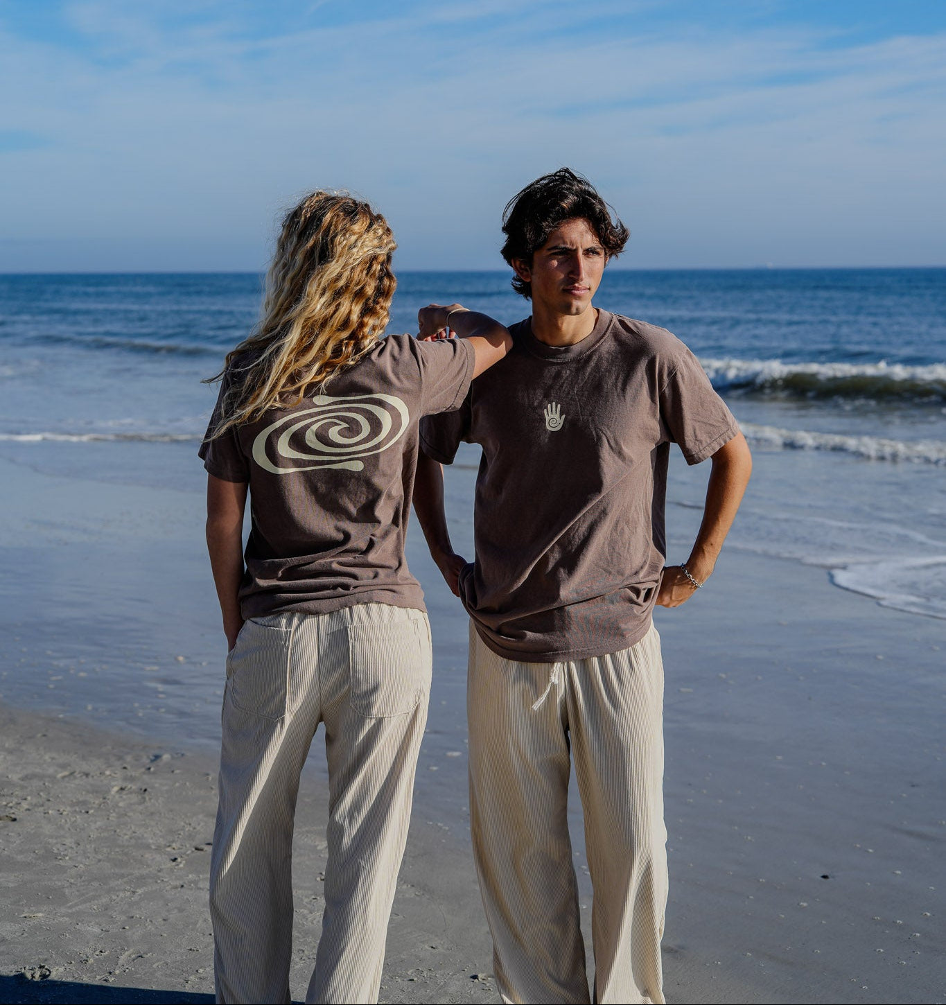 Two people standing on a beach with ocean waves in the background