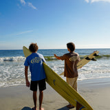 Two people holding surfboards on a beach with clear blue sky and ocean.