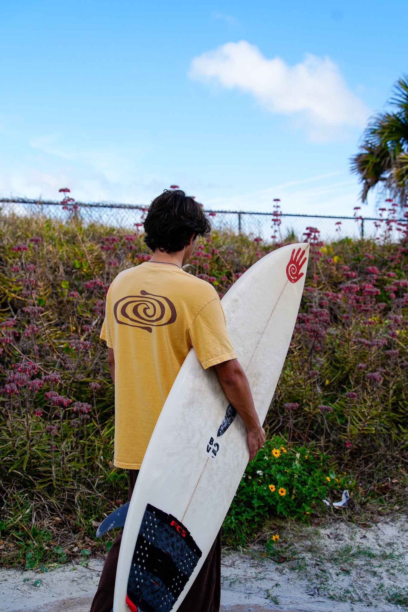 Person holding a surfboard with a spiral design on a beach